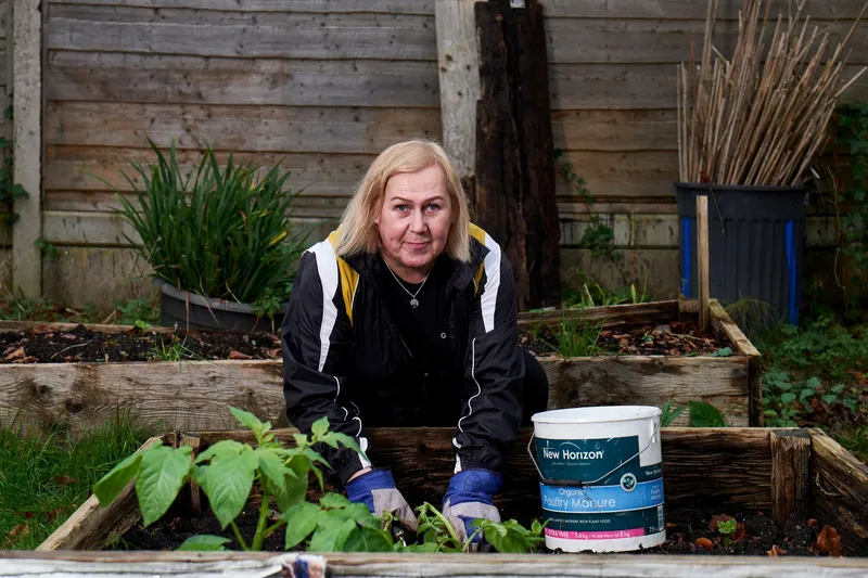 Eine Frau legt ein Hochbeet an und füllt es mit Gartenerde.