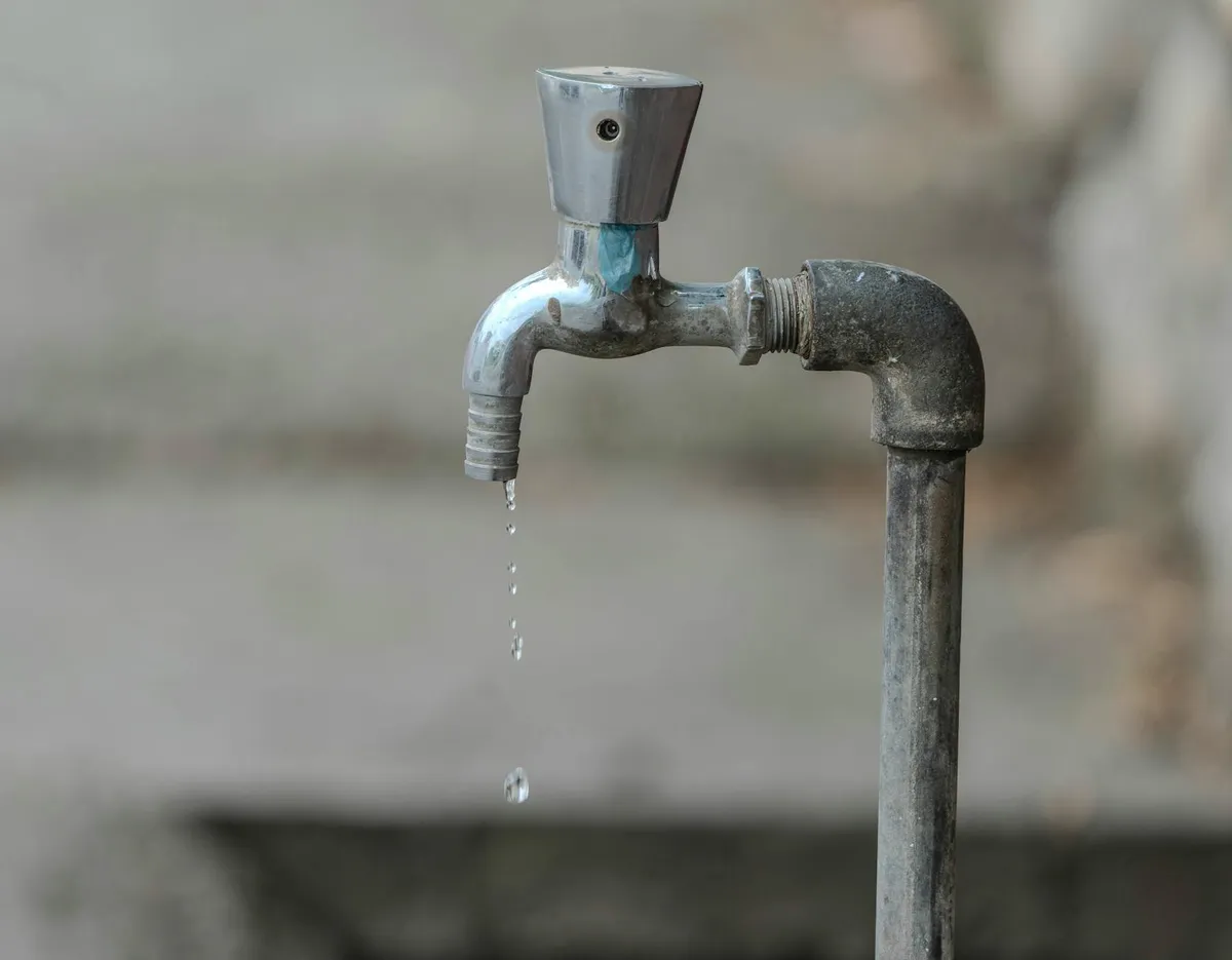 Nahaufnahme eines Wasserhahns im Garten, ein Tropfen fällt von der Öffnung